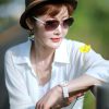 Woman wearing sunglasses and hat holding yellow flower outdoors in bright daylight.
